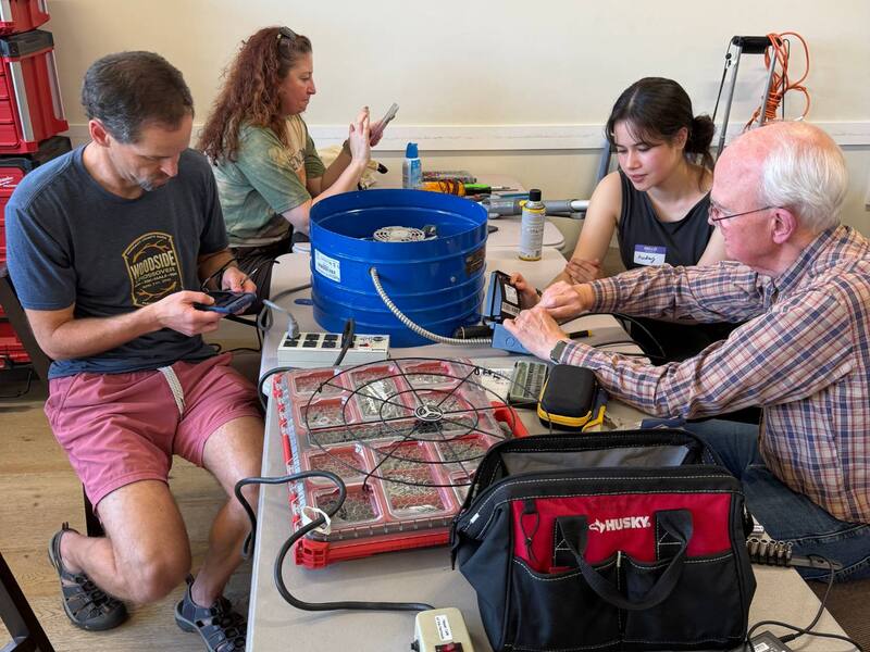Visitors and volunteers working on electronics repairs around a table of tools