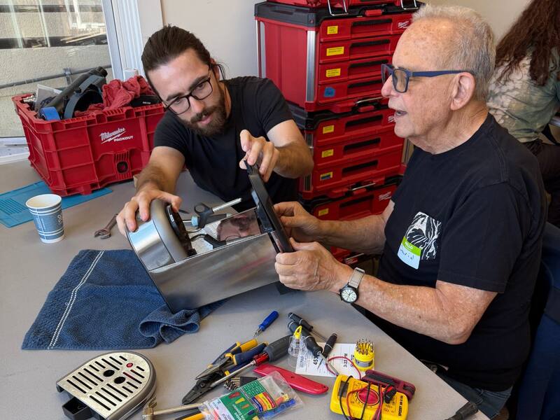A volunteer and a visitor taking apart an espresso machine together