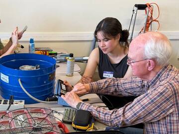 A volunteer and a visitor working on a small electronics repair