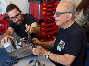 A volunteer and a visitor opening up an espresso machine together