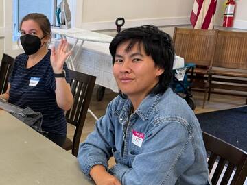 Sewing volunteers waving from the textile repair table